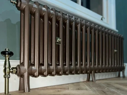 Bronze cast-iron column radiator on a wood floor with traditional valve